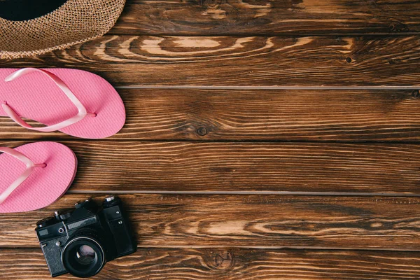 Vista superior de chanclas rosadas, sombrero de paja y cámara de película retro en superficie de madera - foto de stock