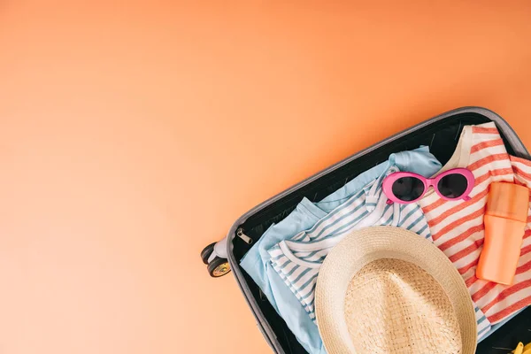 Vista superior de la maleta con accesorios de verano y protector solar sobre fondo naranja — Stock Photo