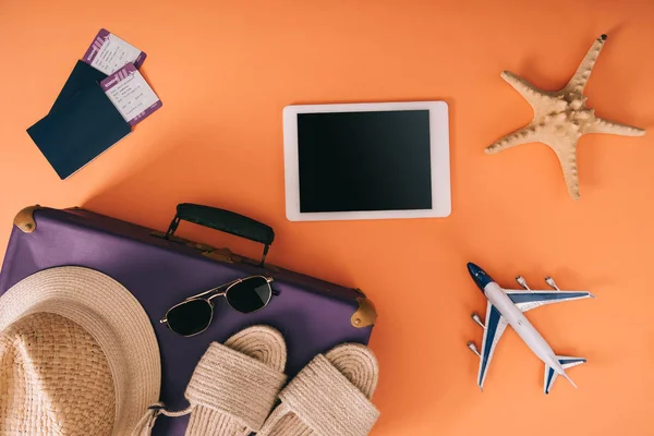 Vista superior de los accesorios de verano en la bolsa de viaje, modelo de avión, tableta digital y pasaportes con billetes en fondo naranja - foto de stock