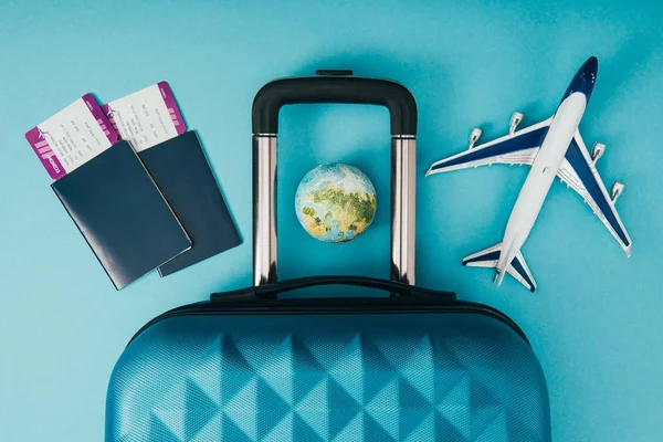 Vue du dessus des modèles globe et avion, sac de voyage et passeports avec billets sur fond bleu — Photo de stock