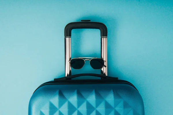 Vista superior de gafas de sol y bolsa de viaje sobre fondo azul - foto de stock