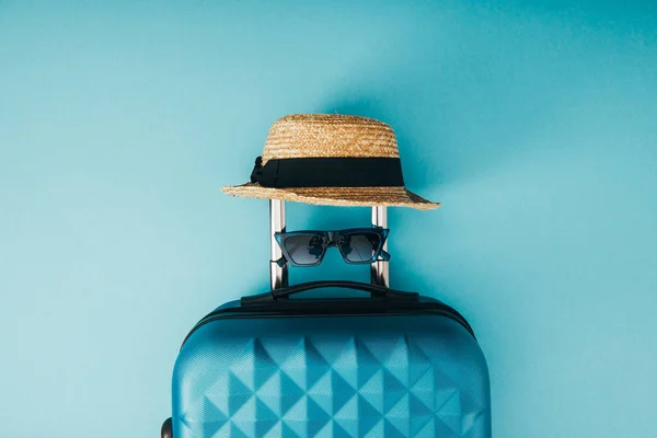 Vue de dessus du chapeau de paille, des lunettes de soleil et du sac de voyage sur fond bleu — Photo de stock