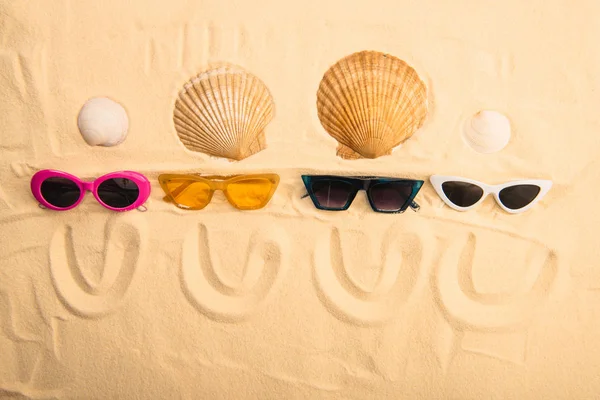 Vista dall'alto di occhiali da sole e conchiglie con sorrisi disegnati sulla sabbia — Foto stock