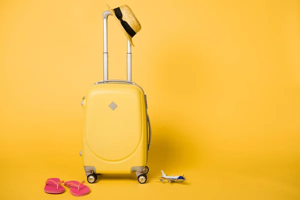 Sac de voyage jaune vif, chapeau de paille, tongs roses et modèle d'avion sur fond jaune — Photo de stock