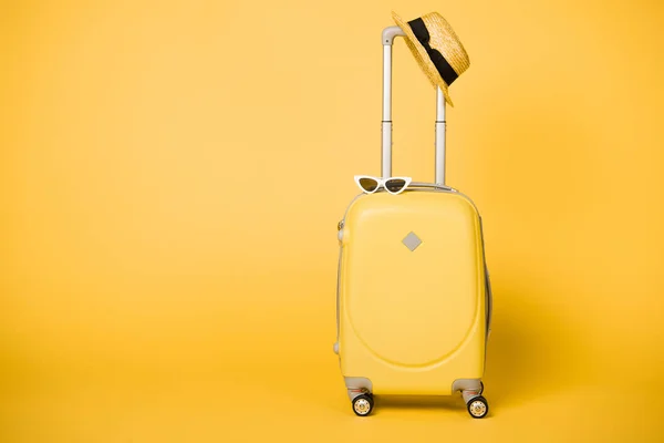 Bright yellow suitcase, sunglasses and straw hat on yellow background — Stock Photo