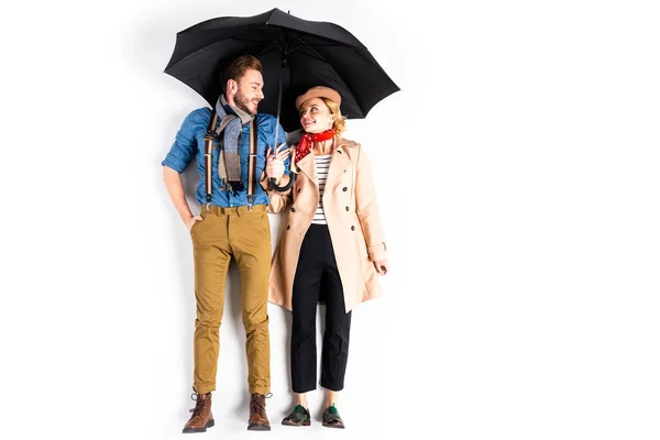 Casal rindo de pé sob guarda-chuva preto e olhando uns para os outros no fundo branco — Fotografia de Stock