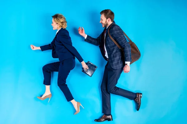 Paar in Anzügen mit Taschen, die gemeinsam auf blauem Hintergrund gehen — Stockfoto