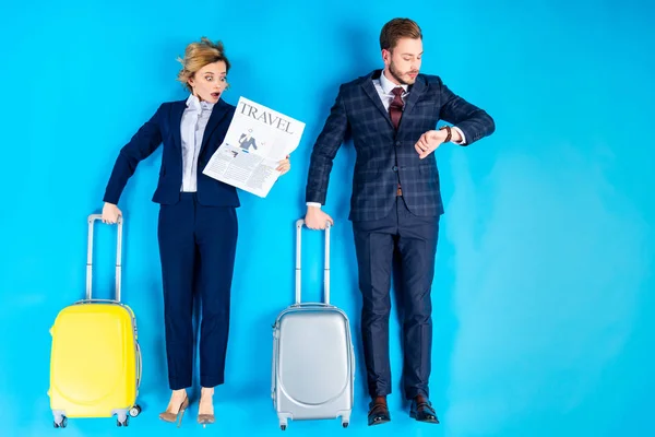 Удивлённая пара с чемоданами, смотрящими на газету и смотрящими на синем фоне — стоковое фото