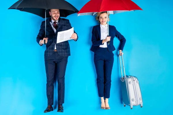 Femme avec valise et homme avec journal debout sous des parapluies sur fond bleu — Photo de stock