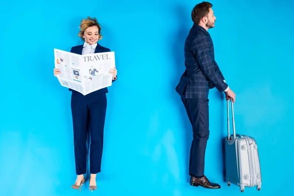 Mujer sonriente leyendo el periódico mientras el hombre de pie con valise sobre fondo azul - foto de stock