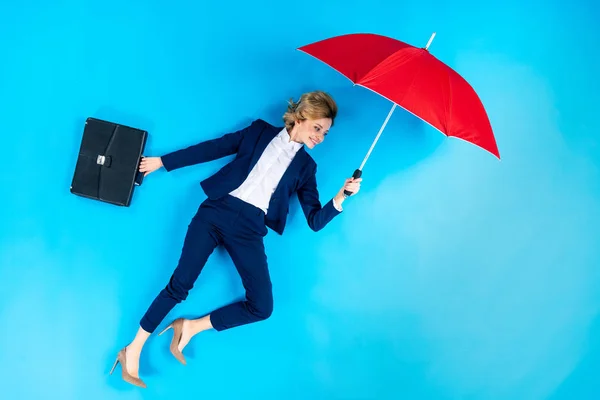 Femme avec mallette posant avec parapluie rouge sur fond bleu — Photo de stock