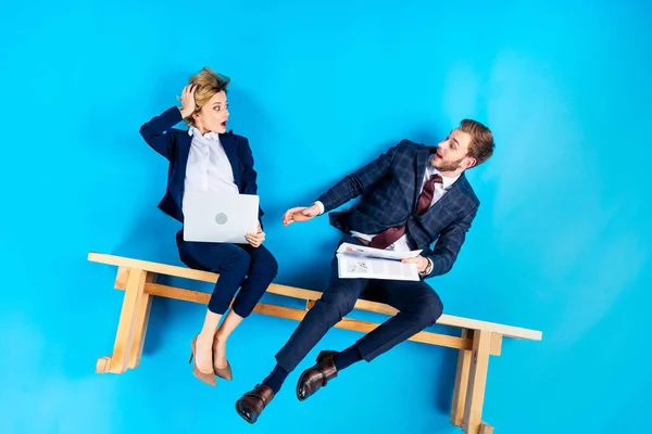 Casal surpreso lendo jornais enquanto sentado no banco no fundo azul — Fotografia de Stock