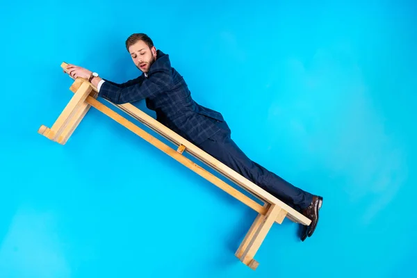 Man in suit lying on wooden bench on blue background — Stock Photo