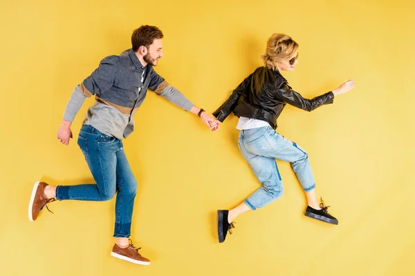 Fashionable couple holding hands and running on yellow background — Stock Photo