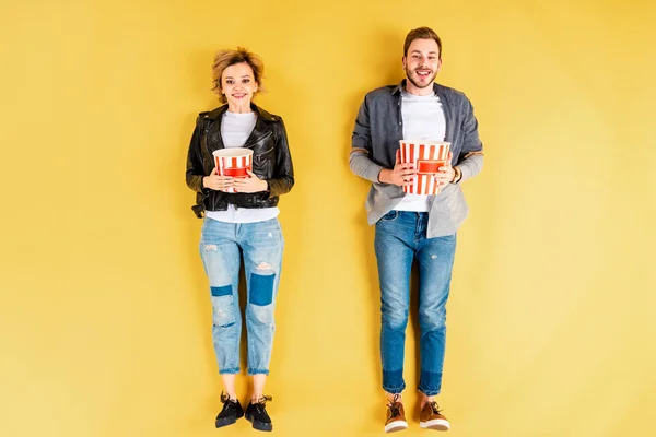 Smiling couple in jeans holding popcorn on yellow background — Stock Photo