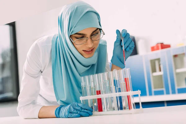 Científica musulmana femenina añadiendo sangre en el tubo de ensayo en el laboratorio - foto de stock