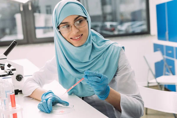 Foco seletivo de sorrir cientista muçulmano feminino no hijab fazendo teste de sangue em laboratório — Fotografia de Stock