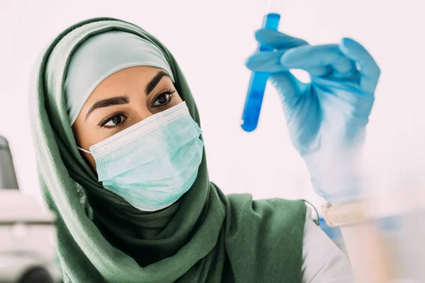 Cientista muçulmano fêmea em máscara médica segurando tubo de ensaio em laboratório — Fotografia de Stock