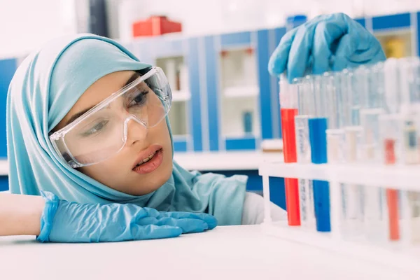 Cientista muçulmano fêmea olhando para tubos de ensaio com líquido vermelho e azul em laboratório — Fotografia de Stock