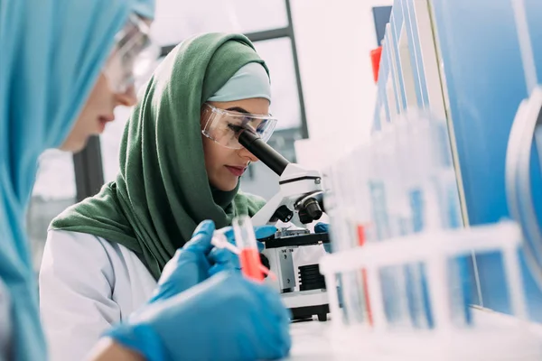 Selective focus of female muslim scientist looking through microscope in chemical laboratory — Stock Photo