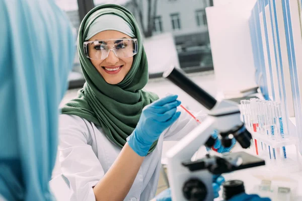 Smiling female muslim scientist in goggles and hijab during experiment in chemical laboratory — Stock Photo