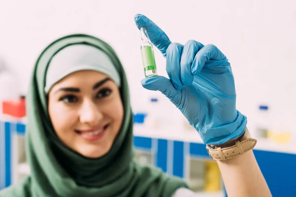 Souriant femme musulmane scientifique tenant ampoule en verre en laboratoire — Photo de stock