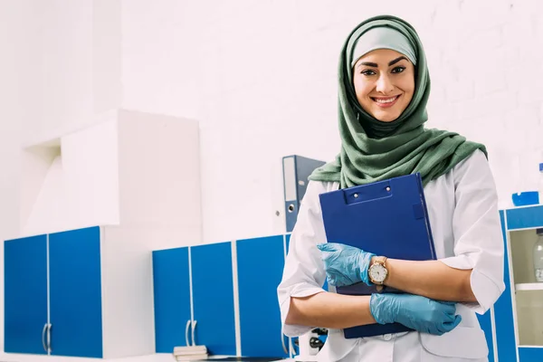 Mujer musulmana científica sujetando el portapapeles y mirando a la cámara en el laboratorio con espacio de copia - foto de stock