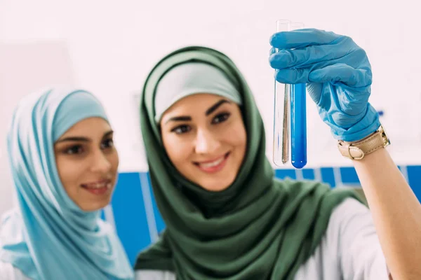 Smiling female muslim scientists holding glass test tubes with reagents during experiment in chemical lab — Stock Photo