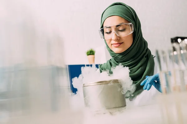 Científica musulmana en gafas durante el experimento con hielo seco en laboratorio - foto de stock