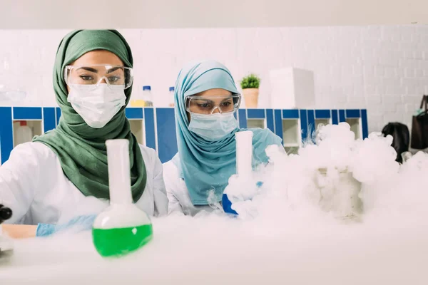 Mulheres cientistas muçulmanas focadas durante o experimento com gelo seco em laboratório químico — Fotografia de Stock