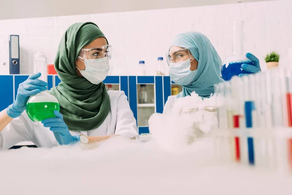 Female muslim scientists holding flasks while experimenting with dry ice in chemical laboratory — Stock Photo