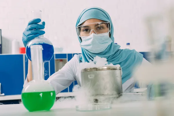 Científica musulmana hembra sosteniendo matraz durante el experimento con hielo seco en laboratorio químico — Stock Photo