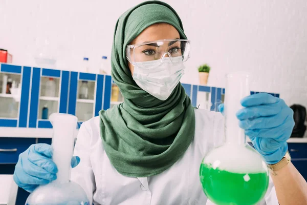 Mujer musulmana científica sosteniendo frascos durante el experimento en laboratorio químico - foto de stock