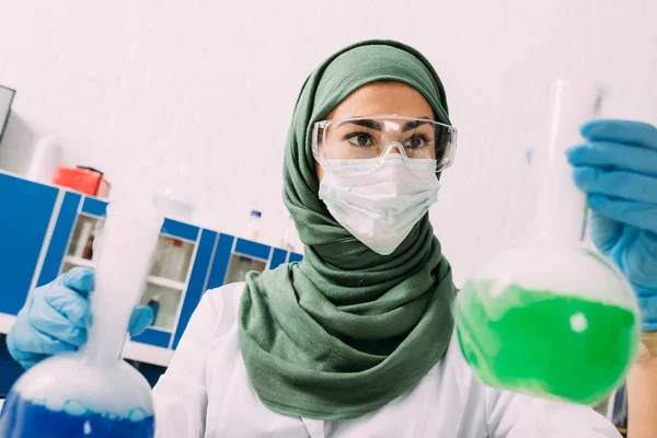 Mujer musulmana científica sosteniendo frascos durante el experimento en laboratorio químico - foto de stock