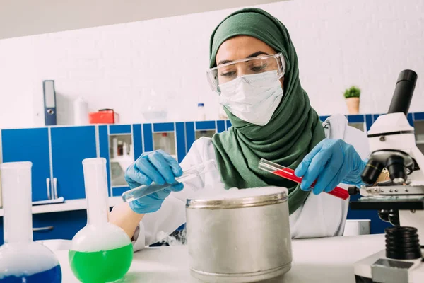 Female muslim scientist holding test tubes over pot with dry ice during experiment in lab — Stock Photo