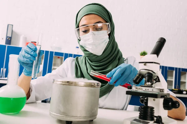 Cientista muçulmano fêmea segurando tubos de ensaio sobre vaso com gelo seco durante experimento em laboratório — Fotografia de Stock