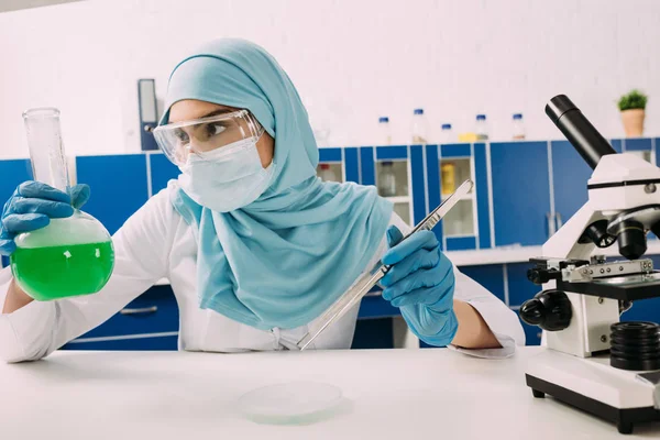 Женщина-мусульманский ученый держит фляжку с пинцетом во время экспериментов с сухим льдом в лаборатории — стоковое фото