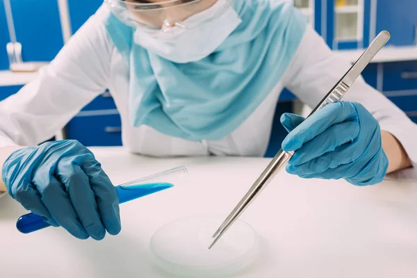 Abgeschnittene Ansicht einer muslimischen Wissenschaftlerin, die Reagenzglas mit Pinzette hält und im Labor mit Trockeneis experimentiert — Stockfoto