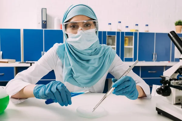 Cientista muçulmano fêmea olhando para a câmera, segurando tubo de ensaio e experimentando com gelo seco em laboratório — Fotografia de Stock