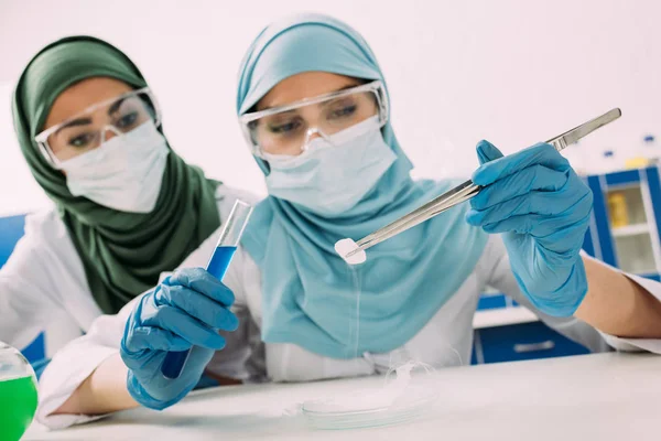 Cientistas muçulmanas fêmeas segurando tubo de ensaio, pinças e gelo seco durante o experimento em laboratório químico — Fotografia de Stock