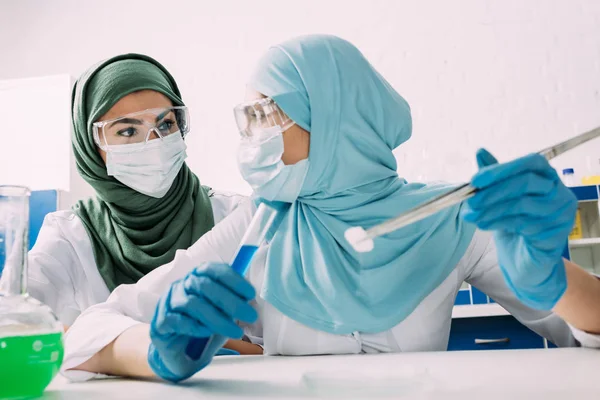 Cientistas muçulmanas fêmeas segurando tubo de ensaio, pinças e gelo seco durante o experimento em laboratório químico — Fotografia de Stock