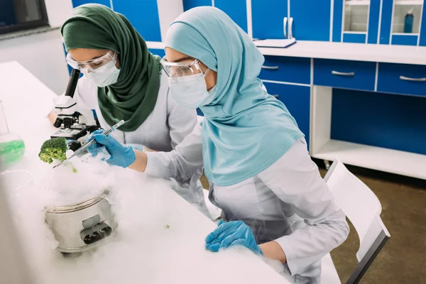 Científicas musulmanas que experimentan con hielo seco y usan microscopio en laboratorio químico - foto de stock