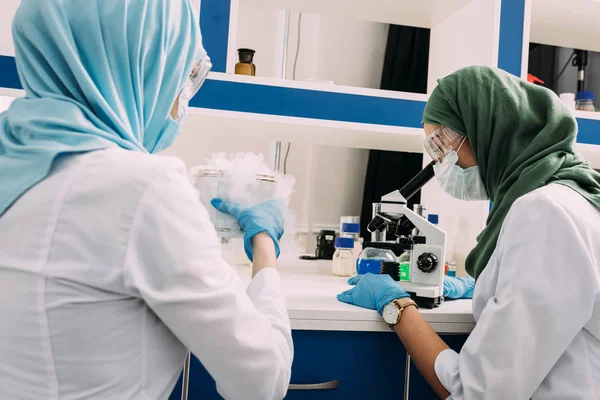 Mulheres cientistas muçulmanas experimentando com gelo seco e usando microscópio em laboratório químico — Fotografia de Stock