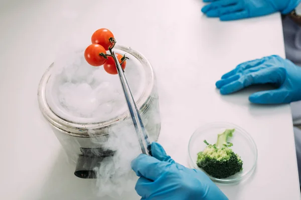 Vista cultivada de cientistas do sexo feminino experimentando com gelo seco e legumes em laboratório químico — Fotografia de Stock