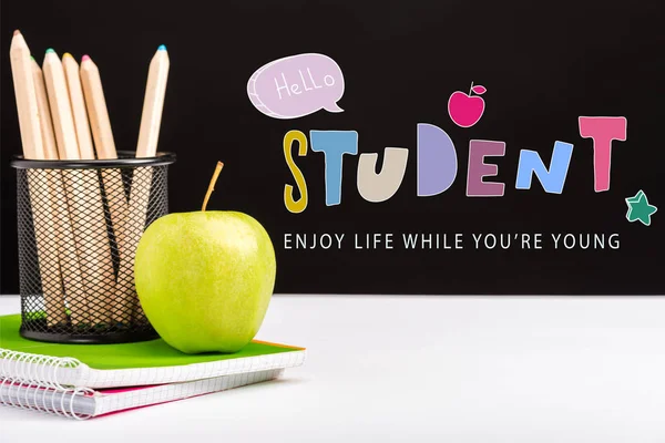 Fresh apple, notebooks and color pencils on table with enjoy life while you are young and hello student lettering on black — Stock Photo