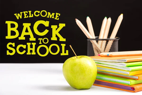 Mela fresca, quaderni e matite a colori sul tavolo con bentornato a scuola lettering su nero — Foto stock