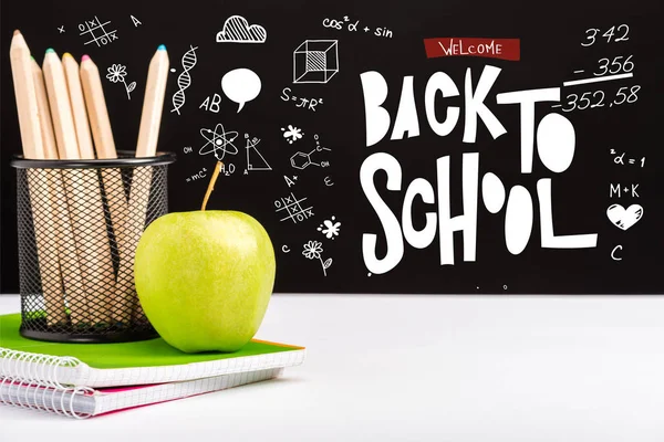 Свіже яблуко, блокноти та кольорові олівці на столі з вітанням назад до шкільного написання та іконки на чорному — стокове фото