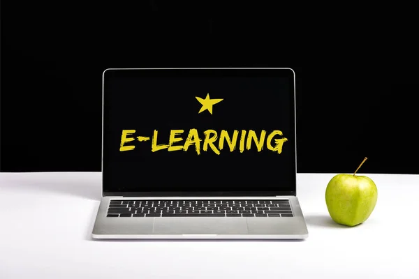 Fresh green apple and laptop on table with e-learning lettering and star on screen isolated on black — Stock Photo