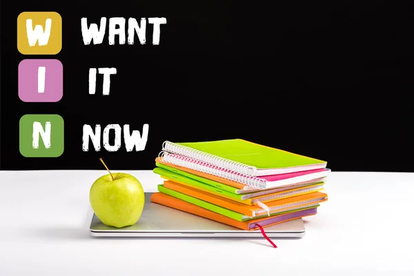 Closed laptop, green apple, notebooks and color pencils on desk with want it now and win lettering on black — Stock Photo