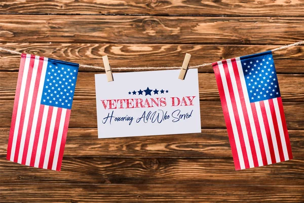 Card with veterans day lettering hanging on string with pins and american flags on wooden background — Stock Photo